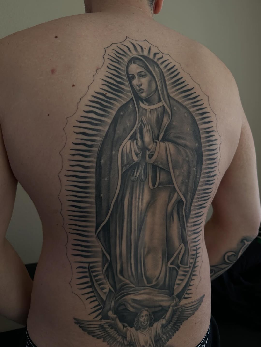 Detail view of La Virgencita religious tattoo with roses by Mauricio Contreras at Broadway Dept