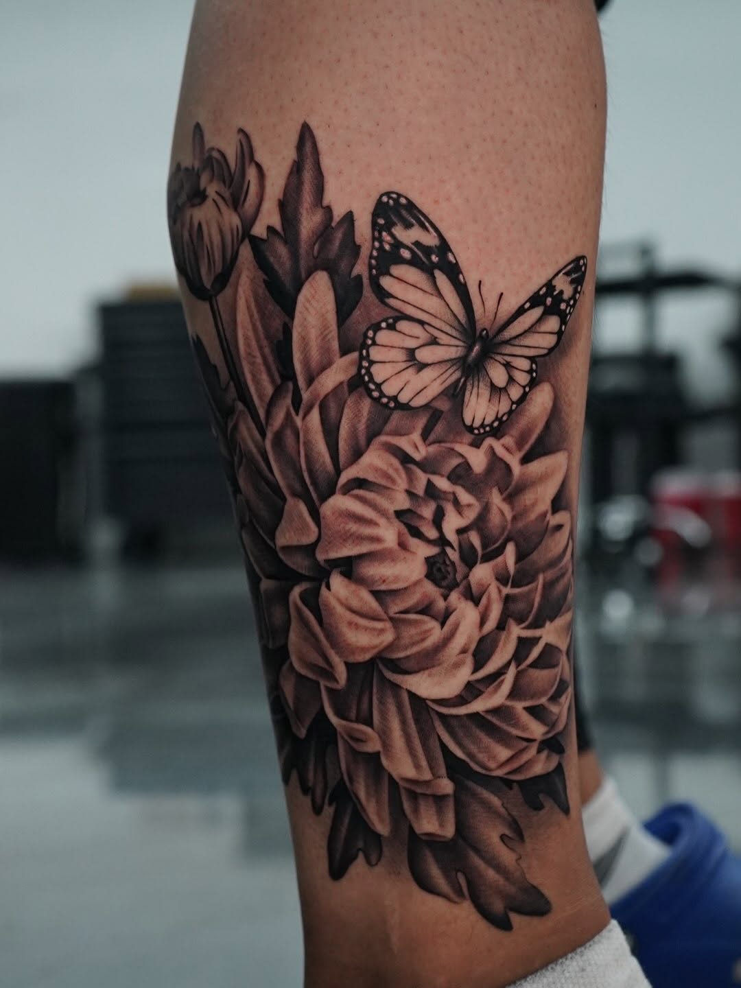 Close-up of chrysanthemum flower tattoo with butterfly detail by Broadway Dept.